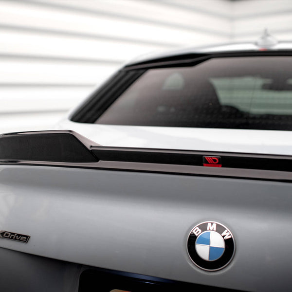 Car trunk showing a "BMW" logo and "xDrive" badge, with a spoiler on the rear. The background consists of white, horizontal panels, suggesting a garage or showroom setting.