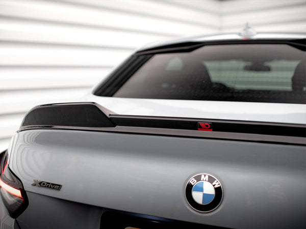 Car trunk showing a "BMW" logo and "xDrive" badge, with a spoiler on the rear. The background consists of white, horizontal panels, suggesting a garage or showroom setting.