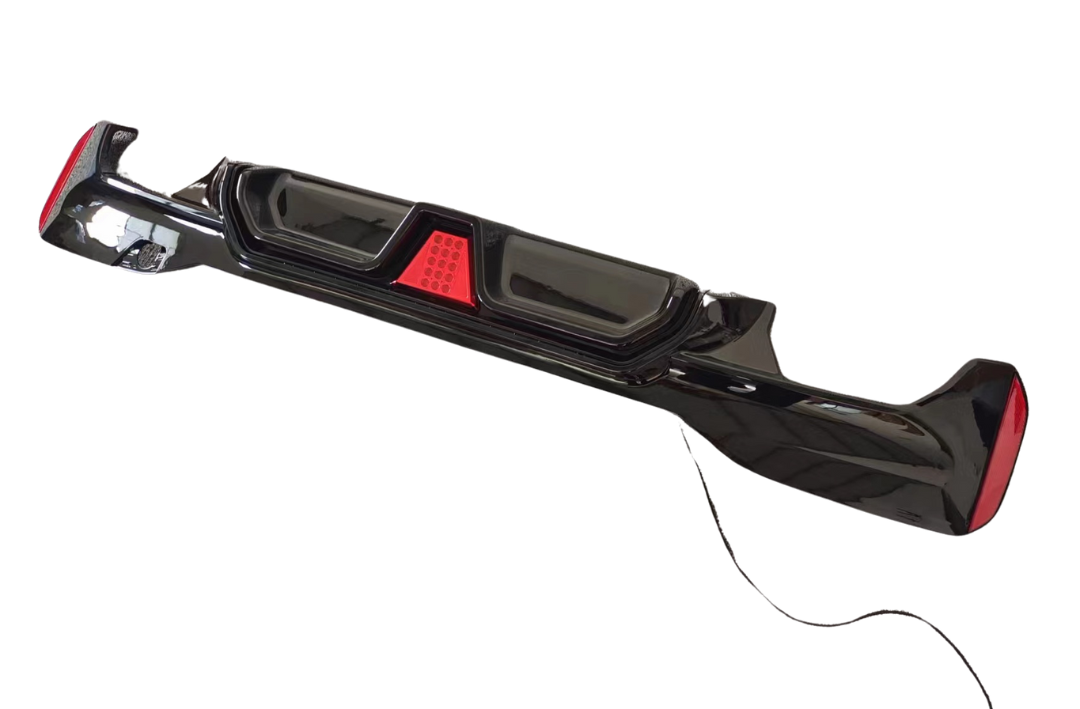A black car bumper with built-in red brake lights, designed to fit at the rear of a vehicle; it lies on a plain white background with an attached cable.
