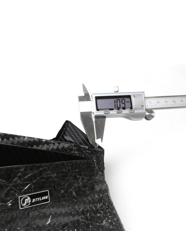 A digital caliper displays "10.9 mm" as it measures the thickness of a black carbon-fiber object. The setting is a clean, white background. Visible text: "Inch/mm OFF ON ZERO", "J's RACING".