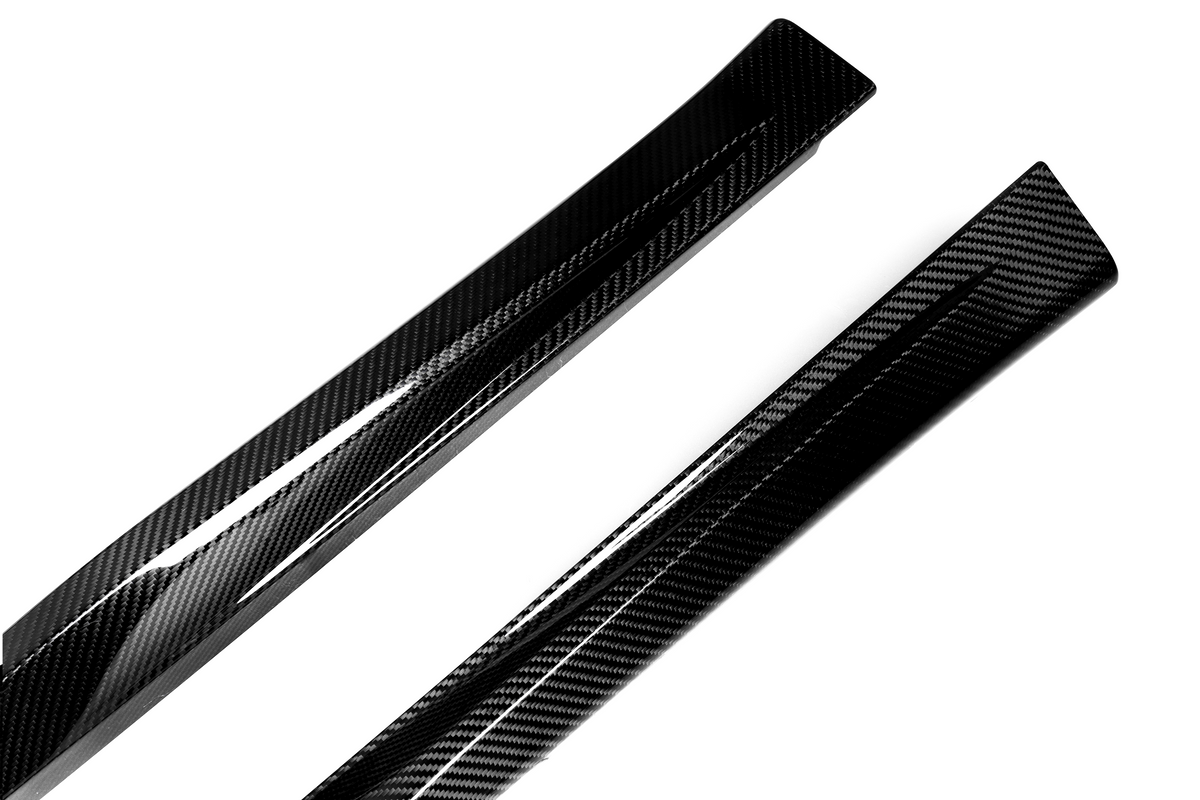 Two sleek carbon fiber components are angled diagonally across a plain white background, showcasing their glossy finish and distinctive woven pattern.