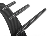 A carbon fiber diffuser with three vertical fins extends outward, angled against a plain white background, showcasing its sleek, aerodynamic design.