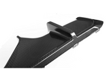 A carbon fiber car rear diffuser with fins is angled upward, showcasing its sleek, aerodynamic design. It is positioned against a plain white background, highlighting its textured surface.