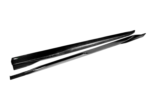 Two sleek, black carbon-fiber side skirts lie parallel on a white background, showcasing their smooth, aerodynamic design ideal for automotive enhancements.