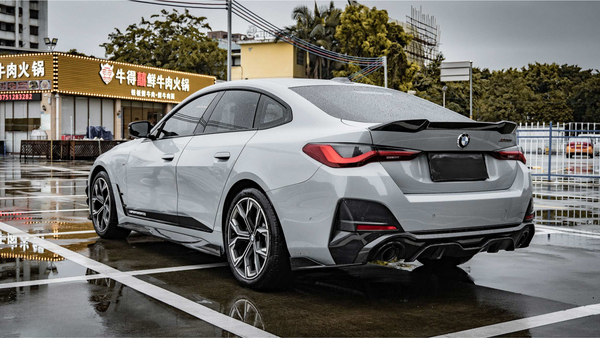 A silver car is parked on a wet pavement near a restaurant with illuminated signage in Chinese characters and telephone numbers: "0752323232" and "075523282".