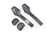 Four black plastic automotive interior panels lie on a white background, including two elongated and two smaller rectangular pieces. Each piece has small white labels or marks.