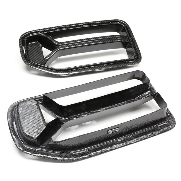 Two black carbon fiber car hood vents lie on a white surface. Each vent has a rectangular shape with a textured finish and features the "RTMG" logo attached.