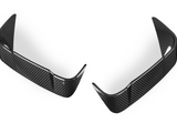 Two carbon fiber car bumper lips are positioned symmetrically. They have a glossy, textured surface and curved edges, set against a plain white background.
