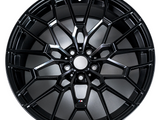 A black alloy wheel features a complex, multi-spoke design. It's displayed against a plain, white background. There is a small logo with the letter 