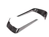 Two curved carbon fiber trim pieces, reflecting light, positioned apart on a white background. They are designed for vehicle detailing.