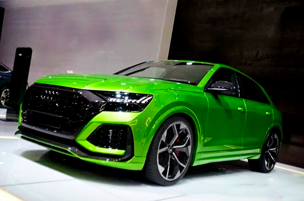 A vibrant green sports car sits angled on a glossy showroom floor, featuring a sleek body, large alloy wheels, and a dark grille, under bright ceiling lighting.