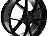 A glossy black wheel rim with a multi-spoke design, resting upright on a plain surface, its sleek finish reflecting light subtly. No text is present.