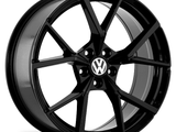A glossy black alloy wheel features a star-shaped, multi-spoke design. The Volkswagen logo is centered on the wheel hub, against a plain white background.