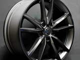 A metallic car wheel rim with a Volkswagen logo, featuring a multi-spoke design, leaning against a gray background. The rim is inscribed with “8Jx20H2, Made in Germany.”