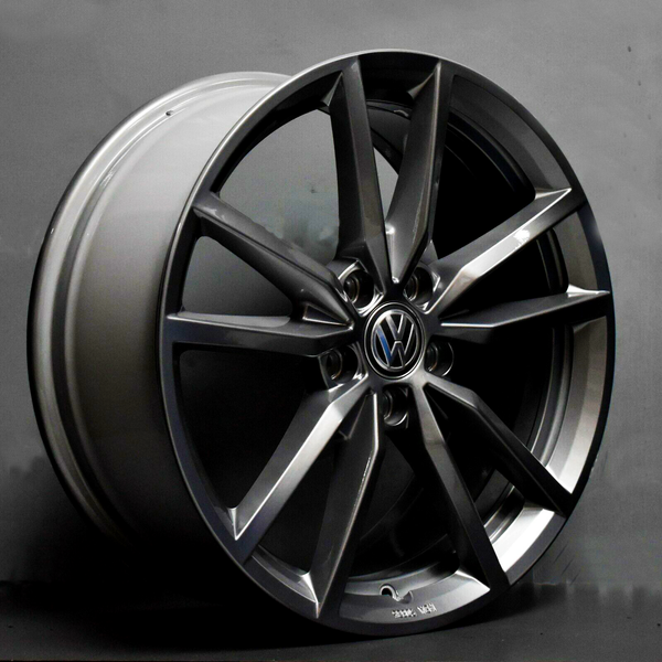A metallic car wheel rim with a Volkswagen logo, featuring a multi-spoke design, leaning against a gray background. The rim is inscribed with “8Jx20H2, Made in Germany.”