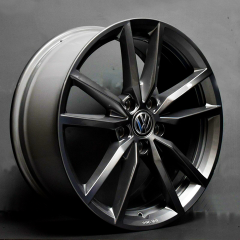A dark gray alloy wheel with a Volkswagen emblem, featuring a multi-spoke design, is positioned against a plain, gray background.