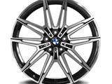 A polished, multi-spoke car wheel rim with a central BMW logo rests against a white background. The design features intricate, symmetrical patterns with alternating black and metallic finishes.