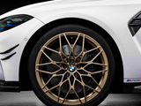 White sports car wheel features intricate gold alloy design with the BMW logo at the center. The car is parked indoors, highlighting details like 