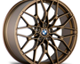 A bronze-colored, intricately designed car wheel rim displays multiple spokes and a central BMW logo. The rim is showcased on a plain, white background.