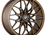 A bronze alloy wheel with geometric spokes features a BMW logo at the center, placed against a plain white background.