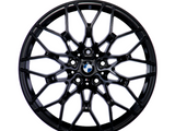 A black, multi-spoke alloy wheel with a central BMW logo, displayed against a plain white background, showcasing intricate design and structure.