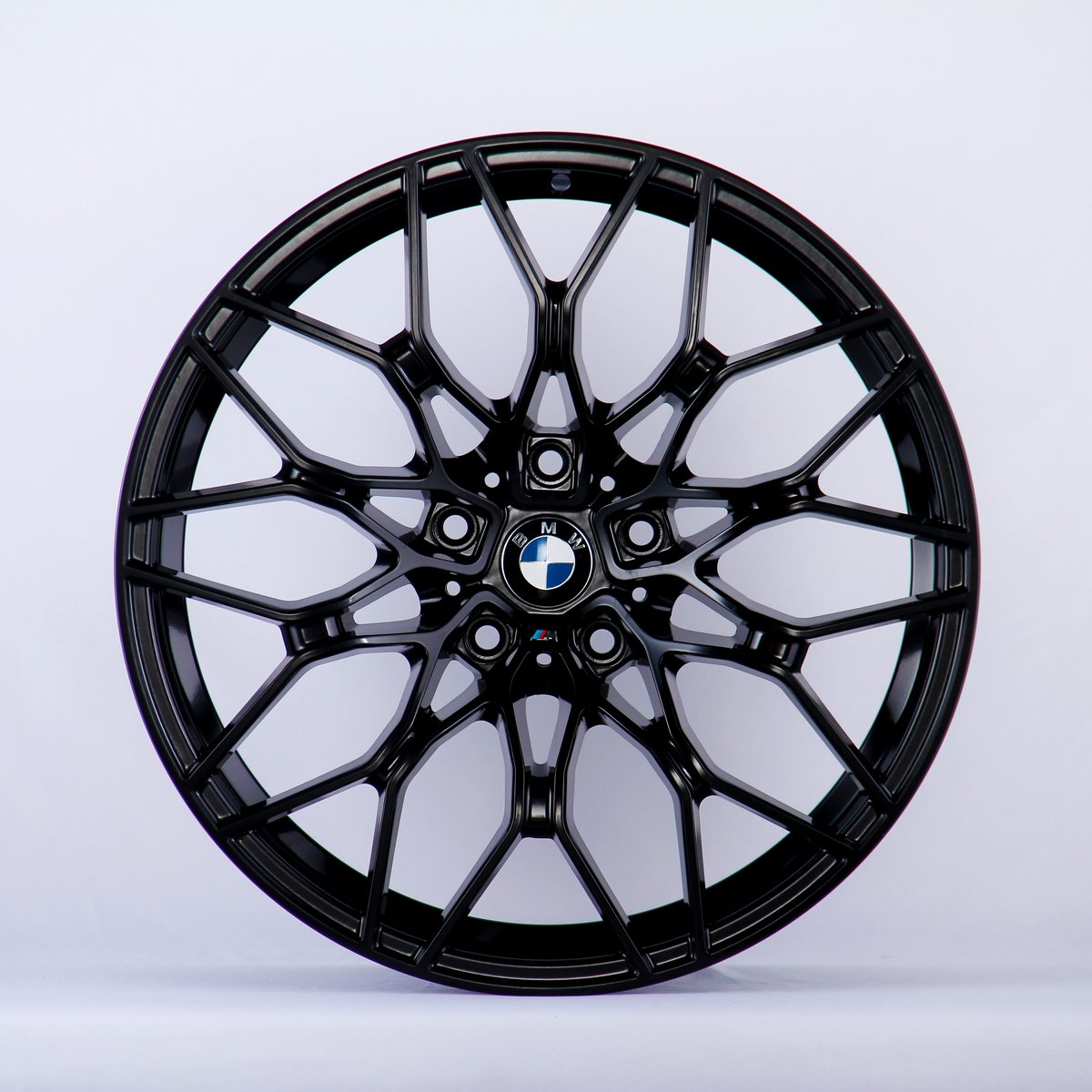 A black, intricately designed car wheel rim with a central blue and white logo is displayed against a plain white background.