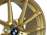 A gold alloy wheel with a five-spoke design prominently features the BMW logo in the center, surrounded by metallic detailing. It is presented against a plain background.