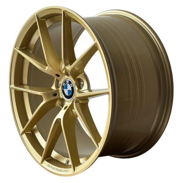 A gold alloy car wheel with a multispoke design features a central BMW logo. It sits isolated on a white background. Text on the rim reads “M PERFORMANCE.”