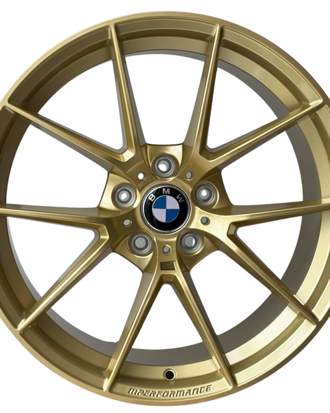 A gold alloy wheel with a black and white BMW logo at the center. The rim is marked "M PERFORMANCE." It features a multi-spoke design against a white background.