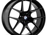 A black, multi-spoke car wheel with a BMW logo in the center rests against a plain white background, displaying a sleek, modern design.