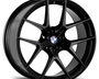 A black, multi-spoke car wheel with a BMW logo in the center rests against a plain white background, displaying a sleek, modern design.