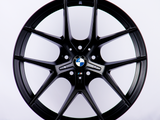 A black car wheel rim with a BMW logo in the center is displayed against a plain white background, emphasizing its sleek, modern design.
