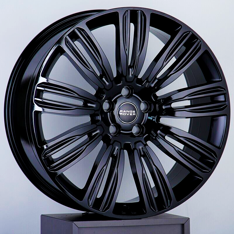 A glossy, black alloy wheel with a multi-spoke design rests on a display stand. The center cap displays the text "RANGE ROVER" in white letters against a dark background.