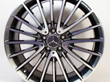 A metallic car wheel with a multi-spoke design features a Mercedes emblem at the center. The word 