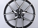 A metallic Mercedes-Benz wheel rim with five intricate spokes showcases the AMG logo, set against a plain white background.