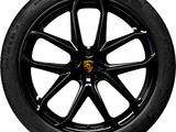 A black car wheel with a multi-spoke rim featuring the Porsche logo in the center. The tire reads 