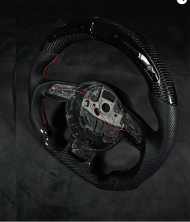 A carbon fiber steering wheel with red stitching and exposed internal wiring, set against a dark background.