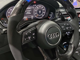 A carbon fiber car steering wheel with buttons is centered in the dashboard of an Audi. Digital displays show 