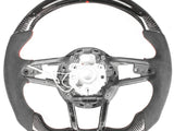 Steering wheel, disassembled, showing a sleek design with carbon fiber and suede accents; some internal wiring is exposed, against a plain white background.