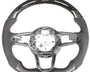 Steering wheel, disassembled, showing a sleek design with carbon fiber and suede accents; some internal wiring is exposed, against a plain white background.