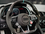 A steering wheel with carbon fiber accents features various control buttons, including 