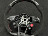 Steering wheel with carbon fiber texture and controls for audio, driving modes, and a red 