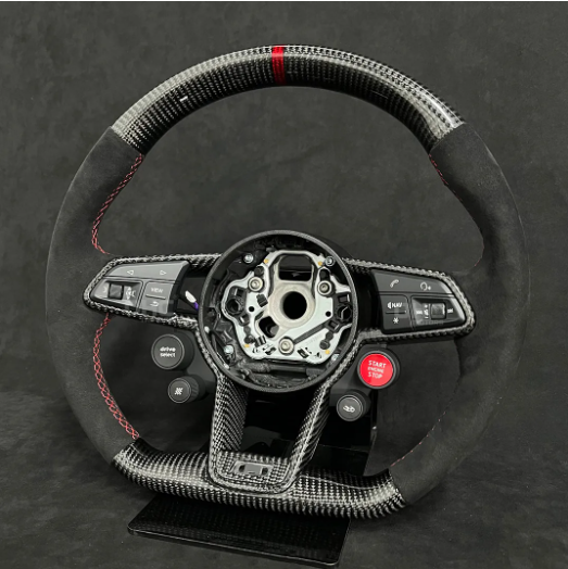 Steering wheel with carbon fiber texture and controls for audio, driving modes, and a red "Start Engine" button, sits against a dark backdrop. Central hub is exposed.