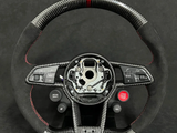 A carbon fiber steering wheel with red accents and buttons labeled 