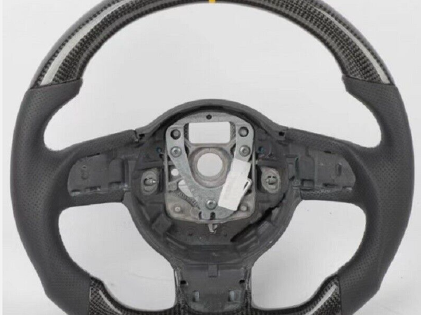 A carbon fiber steering wheel with a yellow stripe at the top, featuring a central mounting area, sits against a plain white background.