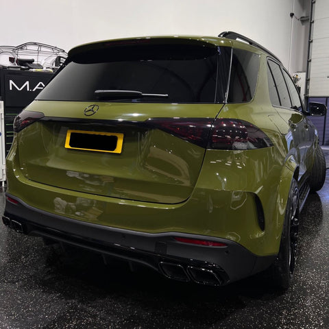SUV parked indoors, displaying a green exterior with dark tinted windows and dual exhaust pipes. Nearby, a black cabinet is labeled "M.A." in a garage setting.