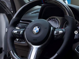 A carbon-fiber steering wheel with a BMW logo is centered in a car's interior, surrounded by a dashboard and speedometer. The text reads: 