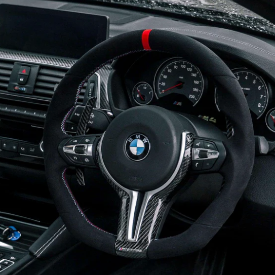 Steering wheel features a BMW logo, carbon fiber accents, and control buttons. The dashboard includes speedometers and a navigation screen, set within a modern car interior on a rainy day.