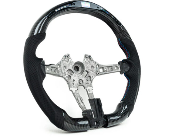 A black carbon fiber steering wheel with a metal frame is displayed against a white background. Blue stitching accents the grip areas, highlighting the sleek, sporty design.