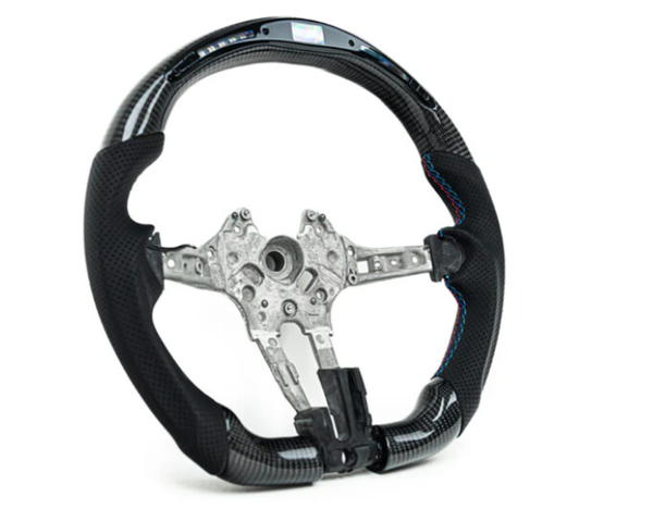A black carbon fiber steering wheel with a metal frame is displayed against a white background. Blue stitching accents the grip areas, highlighting the sleek, sporty design.